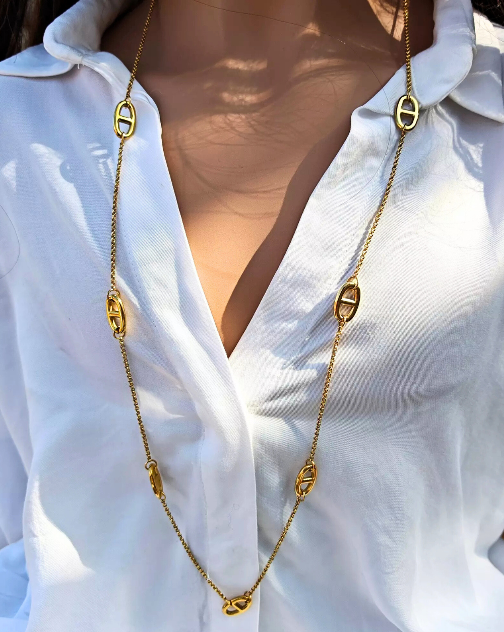 Dolga verižica CHIC iz nerjavečega jekla z razporejenimi členki, prikazana na beli bluz i – Trgovina Patrizia Ljubljana.