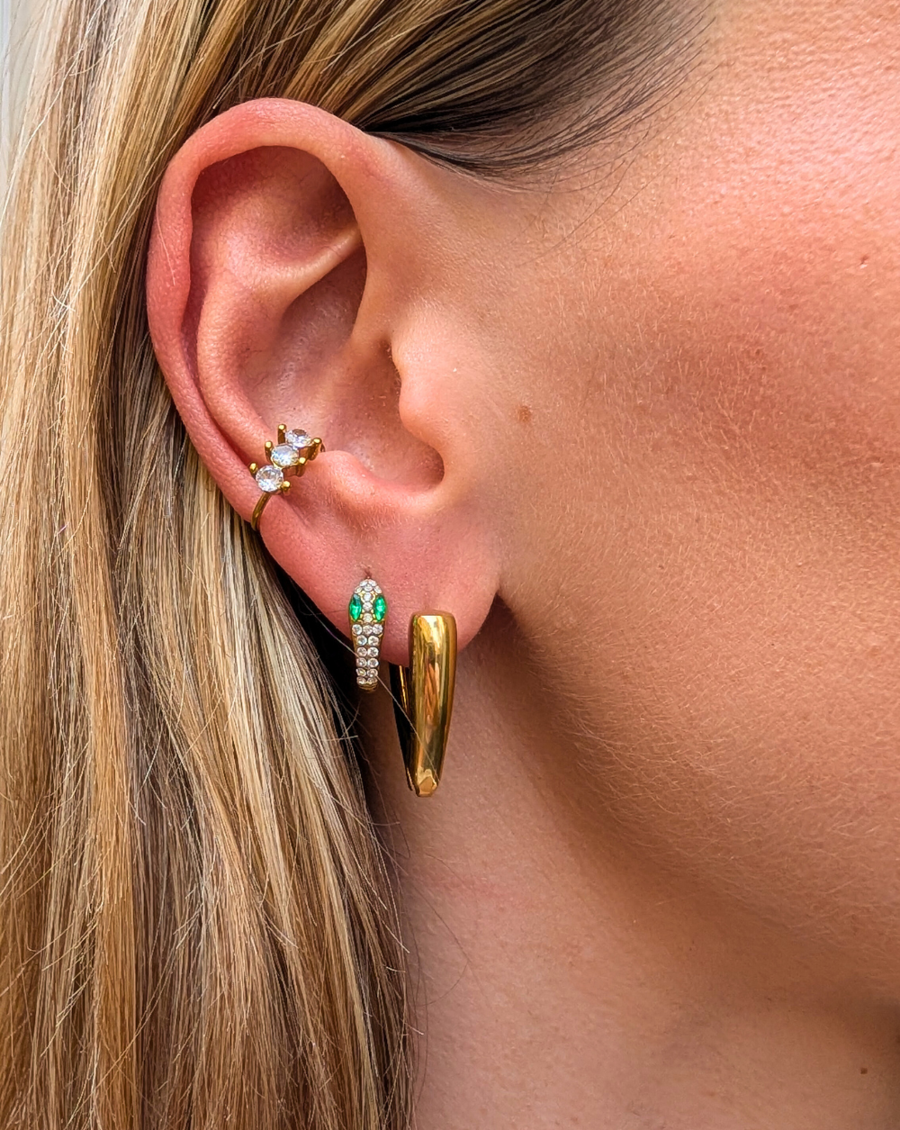 Ein modernes Ohrgehänge mit einer Kombination aus goldenen Ohrringen - ein Schlangenmotiv mit Kristallen, ein minimalistischer Ring und ein Ohrring mit Blattmotiv - aus der Kollektion Patrizia Ljubljana.