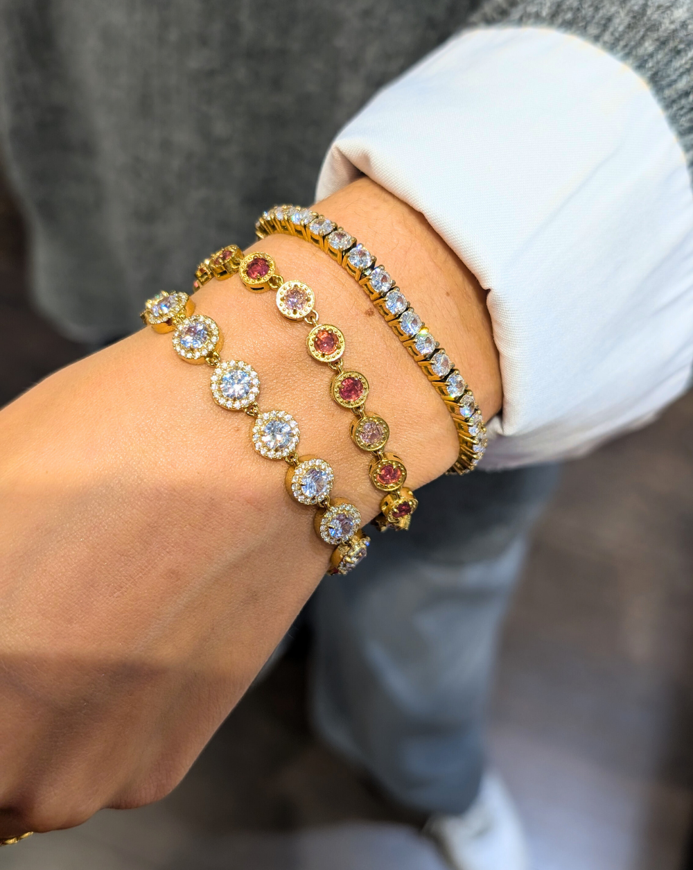 Drei Armbänder aus Edelstahl in Gold - zwei mit runden Zirkonia in klar und rosa und eines mit einem klassischen Set aus weißen Zirkonia, eine elegante Kombination aus funkelnden Patrizia-Schmuckstücken.