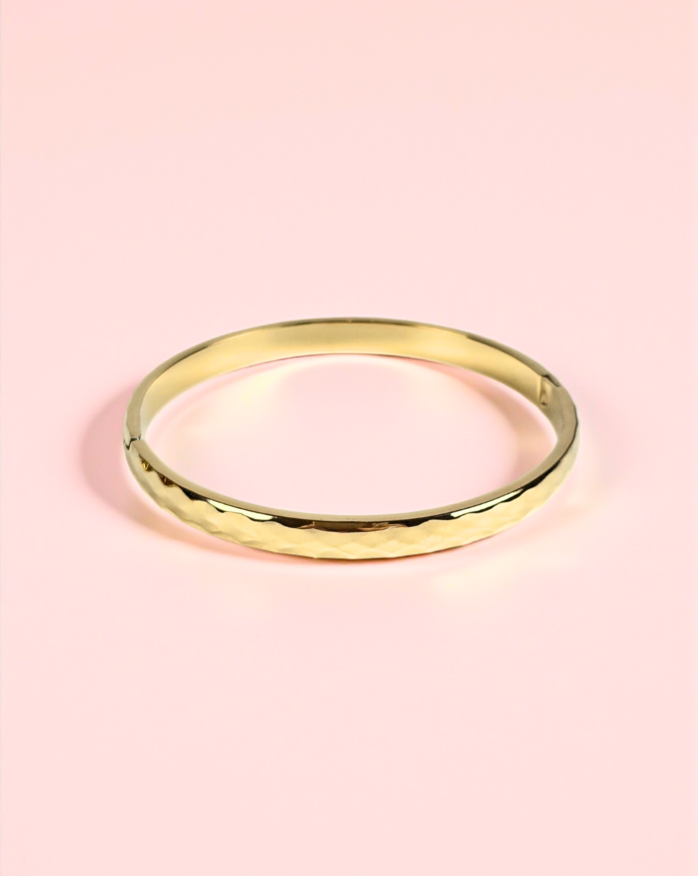 Zlata bangle zapestnica z valovito teksturo iz nerjavečega jekla na rožnatem ozadju – Trgovina Patrizia Ljubljana.