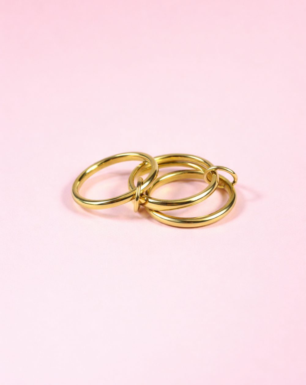 Ring BANDS Gold aus Edelstahl mit drei verbundenen Ringen, fotografiert vor rosafarbenem Hintergrund – Trgovina Patrizia .