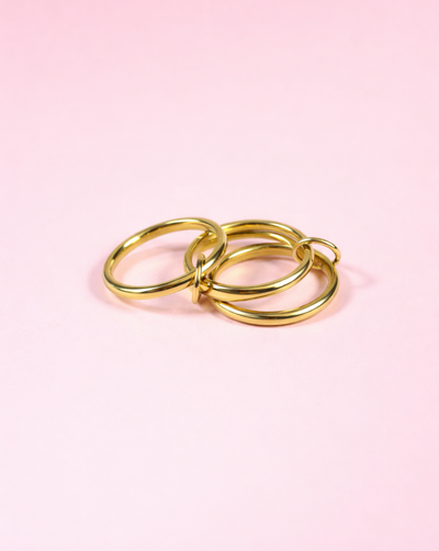 Ring BANDS Gold aus Edelstahl mit drei verbundenen Ringen, fotografiert vor rosafarbenem Hintergrund – Trgovina Patrizia .