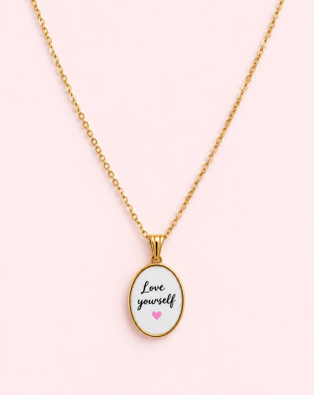 Gold necklace LOVE "YOURSELF" made of stainless steel with an oval white pendant, the inscription " Love yourself," and a tiny pink heart— Trgovina Patrizia , Ljubljana.